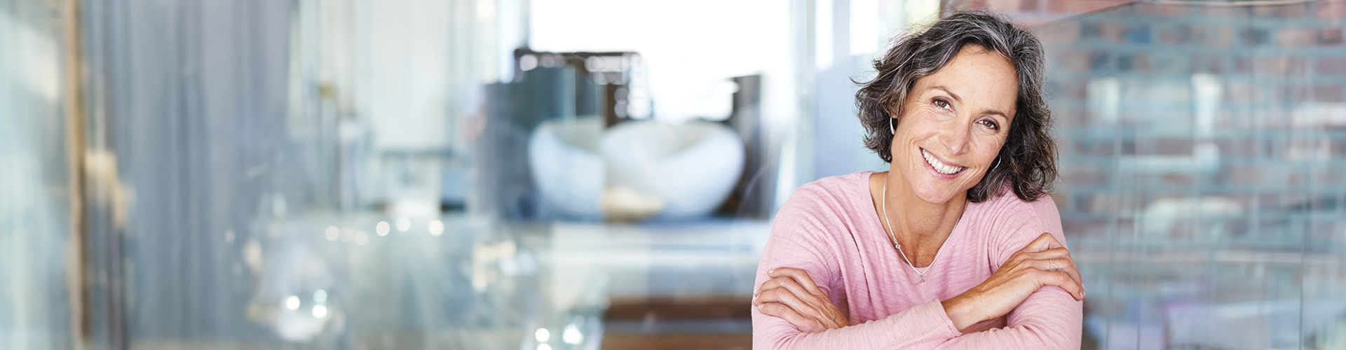 A smiling woman with curly hair resting her arms on a countertop in a bright dental office.
