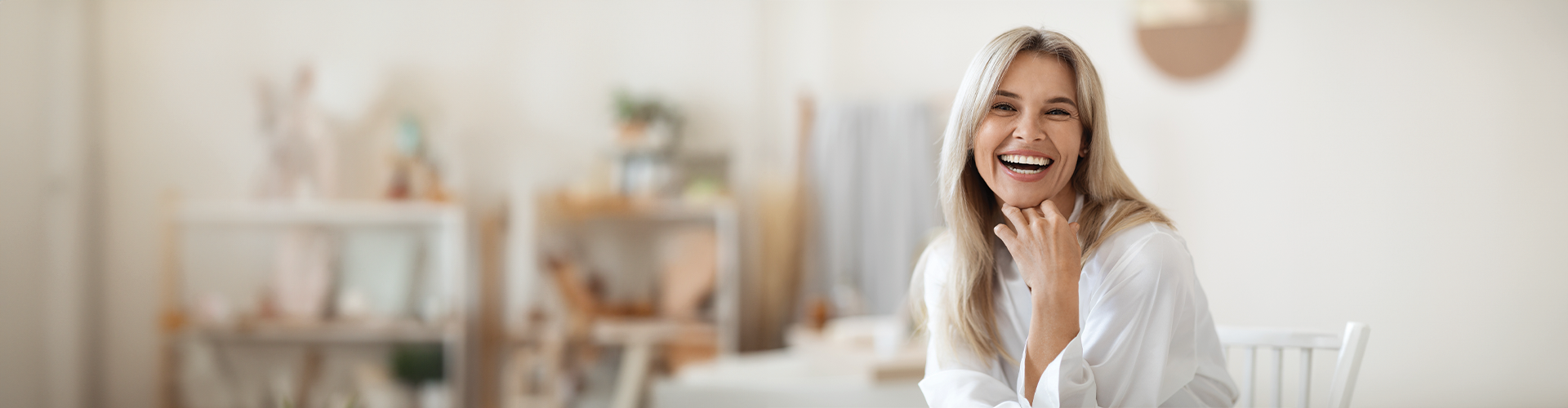 A woman with long, straight hair smiles warmly while sitting in a bright, modern dental office.