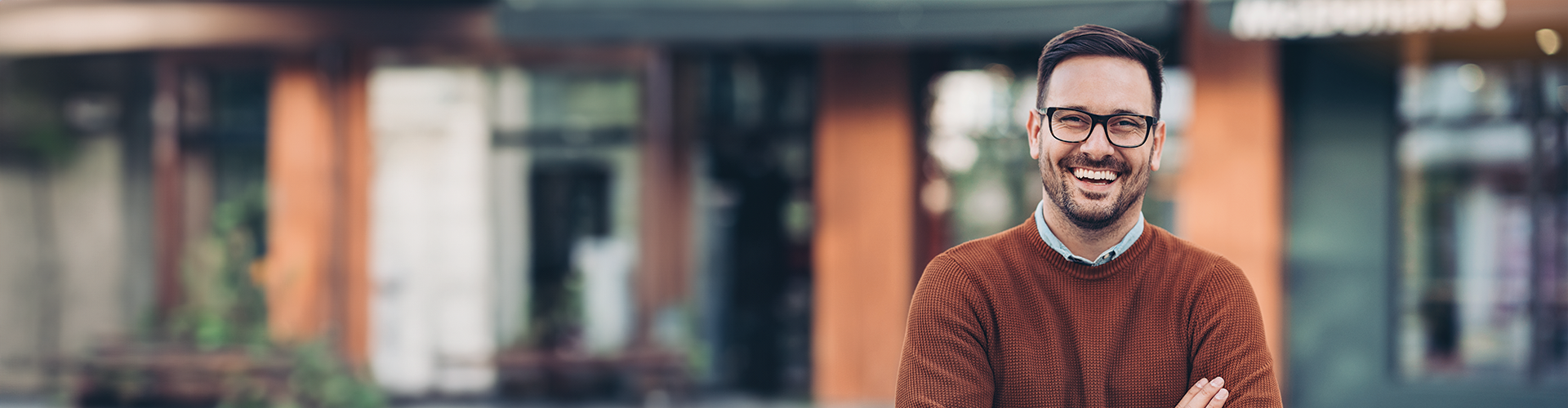 A smiling man with glasses stands confidently in front of a modern building in Colorado Springs.
