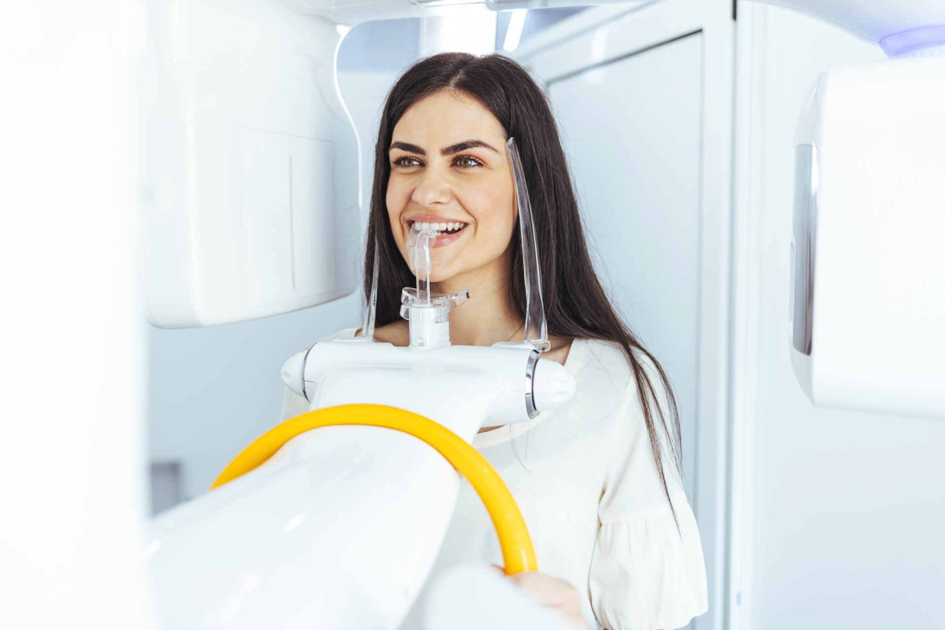A patient smiling while undergoing a dental X-ray in a modern treatment room.
