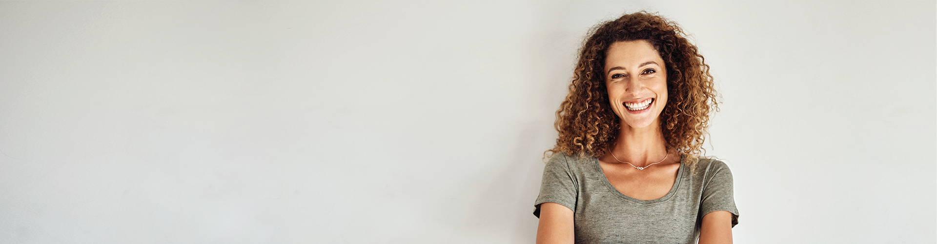 A woman smiling widely against a plain white background, conveying a welcoming and friendly demeanor.