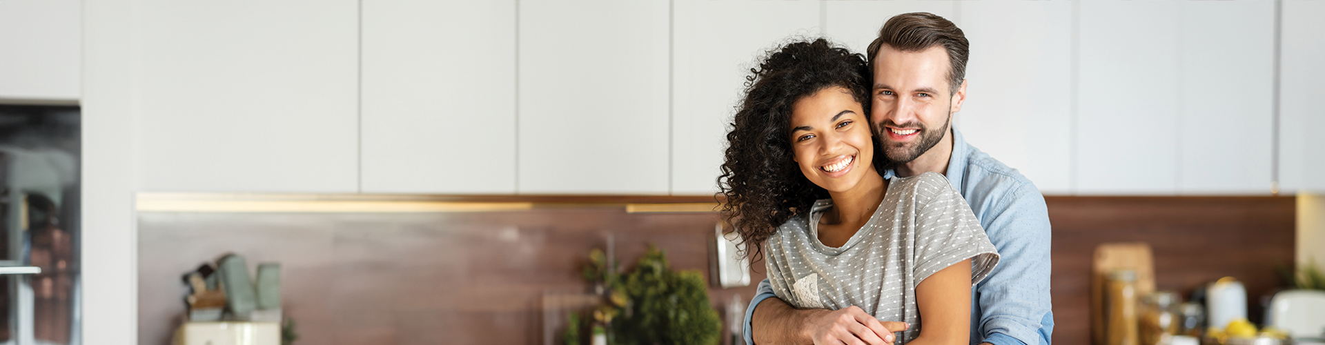A smiling couple embraces in a modern kitchen, exuding warmth and happiness.