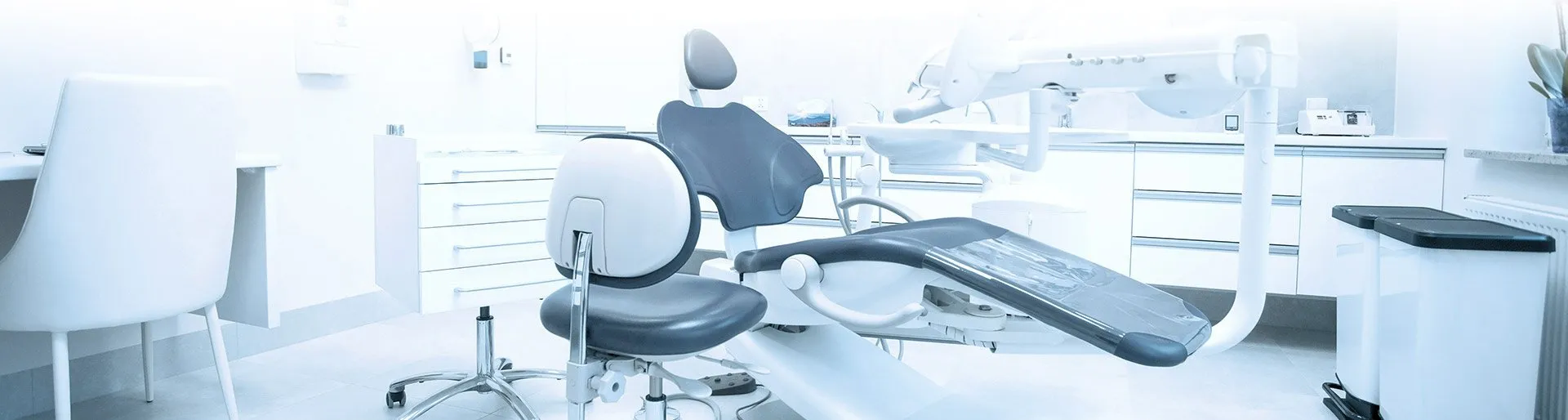A bright dental treatment room featuring a dental chair, stool, and modern equipment arranged neatly.