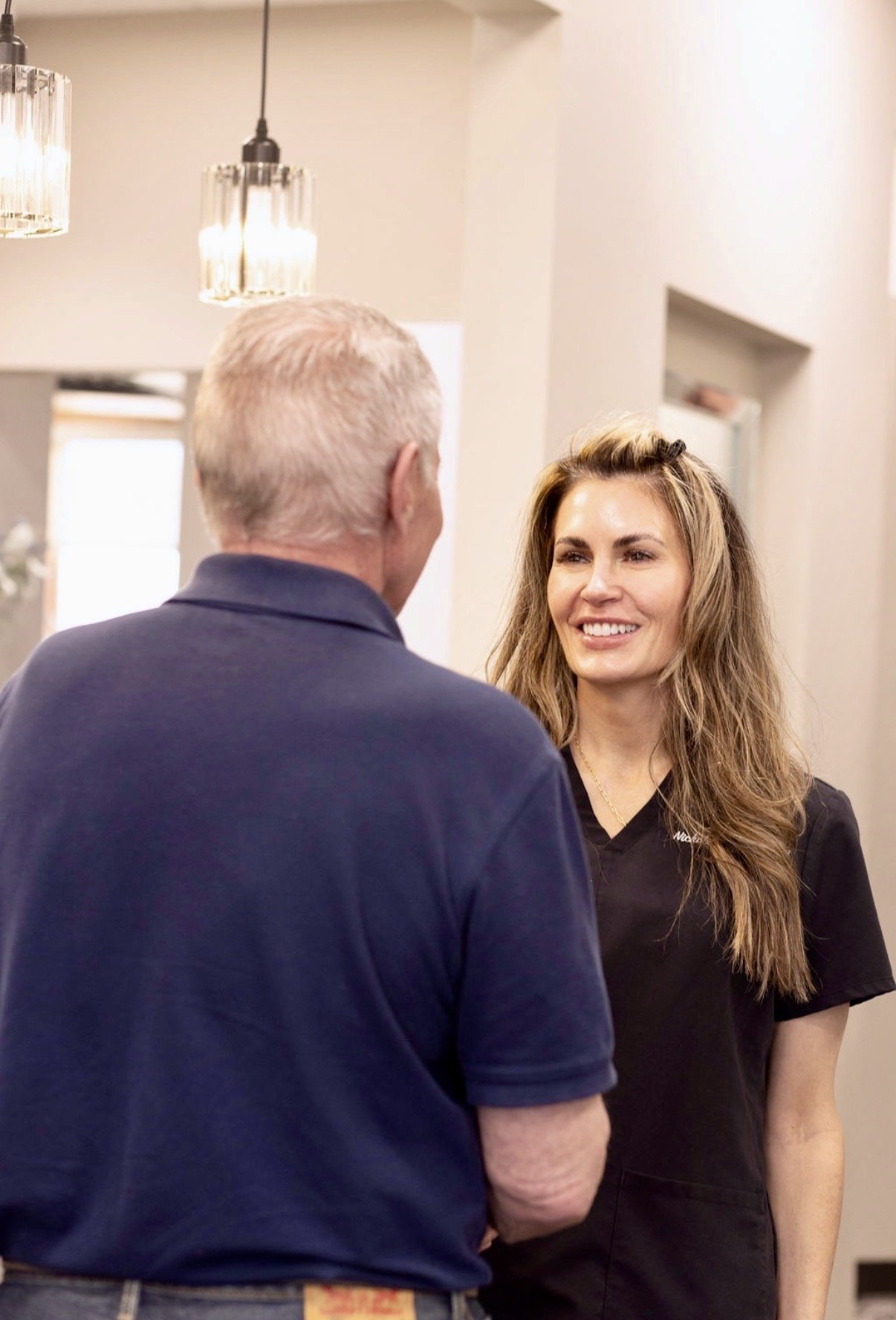 A dentist in a black uniform smiling and engaging in conversation with a male patient in a brightly lit reception area.